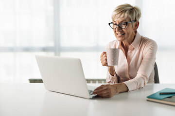 Mature businesswoman drinking coffee while surfing the Internet on a computer in the office