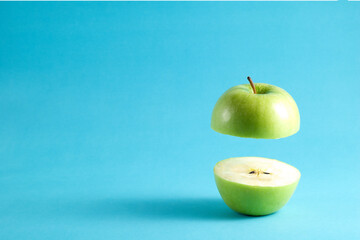 Fresh green apple with a half flying on blue background. Flying green apple with empty copy space for text.