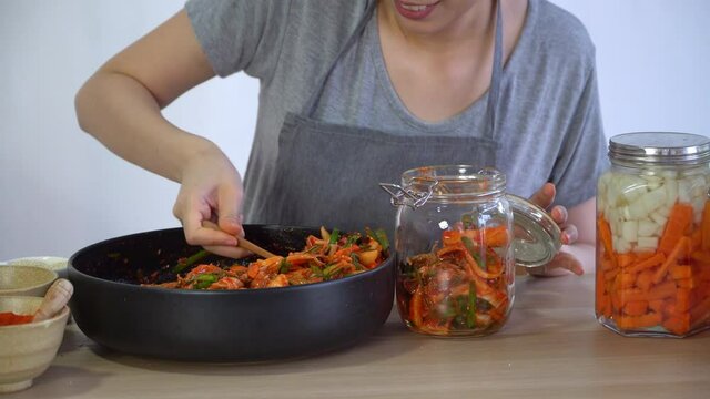An Asian woman making kimchi and putting kimchi in bottles. After learning to cook at home