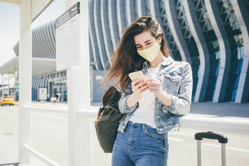 Woman with protective mask standing and using phone at the transport stop, waiting for the tram or...
