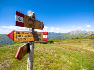 Alpine crossroad with signs indicating to hikers directions and distances to world famous peaks and huts through waymarked trails surrounded by green meadows. Tuscany Apennines. Emilia Romagna. Italy