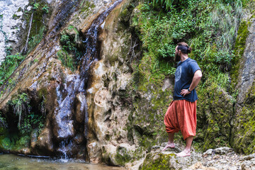 Caucasian man with beard and long hair looking at the water and smiling next to a waterfall and a lake in the Sierra de Tramuntana, Palma de Mallorca, Spain (Copyspace)
