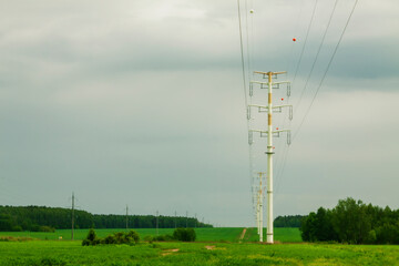 High voltage line with pillars against the background of the forest, field and sky.