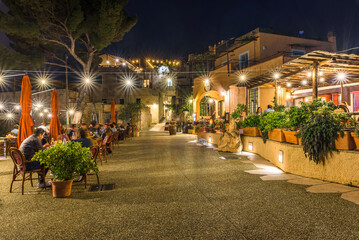 Fototapeta na wymiar Borgio Verezzi, Italy. May 22th, 2021. Lights of the restaurants in Via Roma in the ancient village with people sitting at the tables outdoors.
