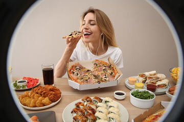 Food blogger eating at table against beige background, view through ring light. Mukbang vlog