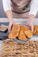 Woman with plate of fried bread with milk, egg, sugar and cinnamon (Torrijas). Typical Spanish Easter sweet. Traditional home cooking concept. Vertical photography and selective focus