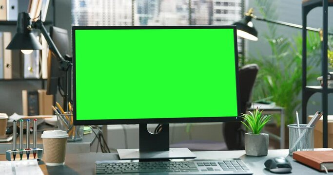 Wide green mock-up screen desktop computer standing on the desk in the modern creative office with bright creative loft for developers and designers where professional working at the background