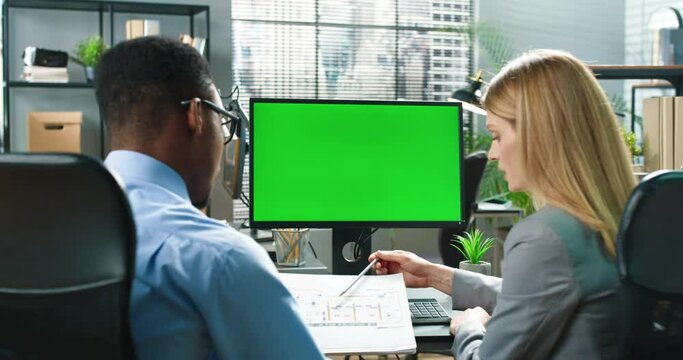 People going about their business at the break. Handsome multiracial man sitting with his colleague and discussing in front of the computer with green screen