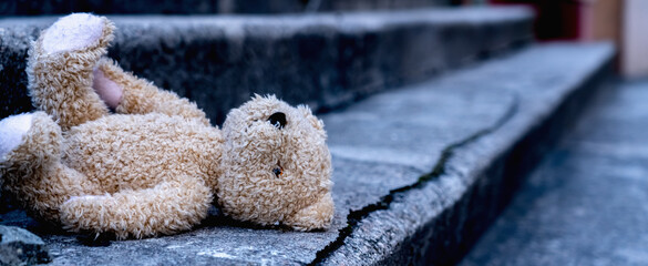 Lost childhood, loneliness and pain concept. Dirty teddy bear lying down outdoors. Horizontal...