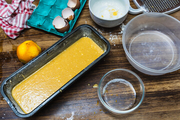Chocolate cake in the bowl before baking, on the table with eggs, orange and various containers