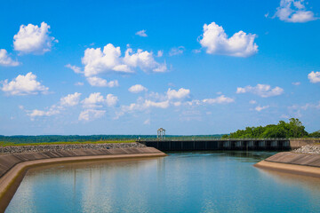 river dam water reservoir lake with surrounding walls and bright blue sunny sky and clouds reflection