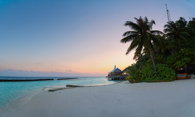 Amazing wide panorama of tropical Maldives island. Exotic beach background with blue lagoon, turquoise water and palm trees during beautiful sunrise. 