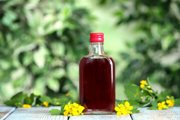 Bottle of celandine tincture and plant on white wooden table outdoors
