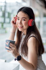 Young Asian woman drinking coffee at a café with wear headphones a wristwatch a coffee cup. Looking at the camera.