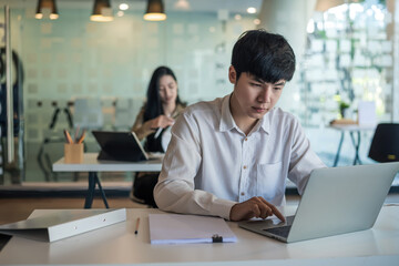Front view of an Asian businessman sitting working on a laptop with blurry back.