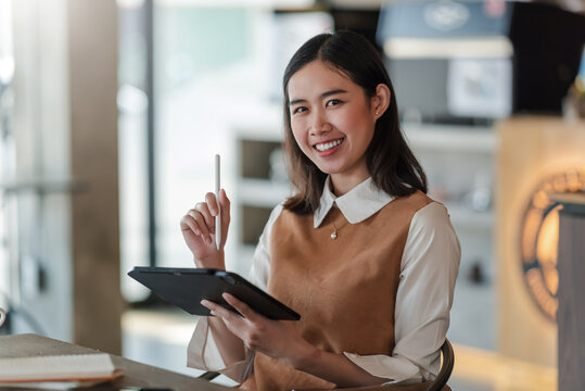 Asian happy smiling woman holding a pen and tablet sitting at a café. Looking at camera.