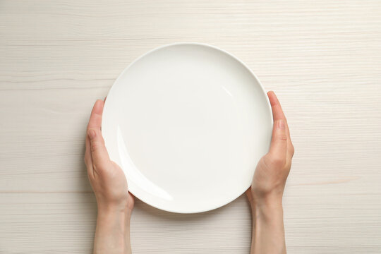 Top view of woman holding empty plate at white wooden table, closeup