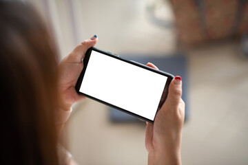 Close-up of a woman hand holding a smartphone horizontally with a blank white screen. Mock up.