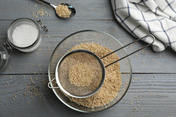 Sieve with rice in bowl on grey wooden table, flat lay