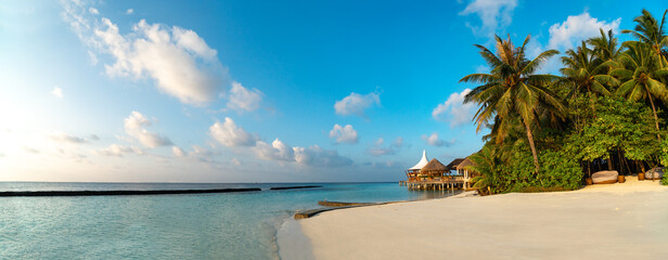 Obraz na płótnie Canvas Amazing wide panorama of tropical Maldives island. Exotic beach background with blue lagoon, turquoise water and palm trees during beautiful sunrise. 