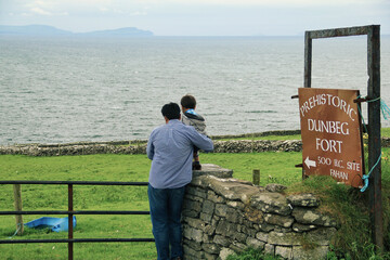 Man and a child standing near to a sign Board at the entrance of Prehistoric Dún Beag fort in Dingle Peninsula, Ireland