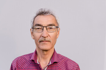 portrait of a mature male pensioner aged 60 with a mustache on a gray background. the face of a...