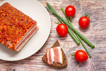 Smoked spicy bacon on a plate. Slice of smoked pork meat on bread, cherry tomatoes and green onion on wooden table. 