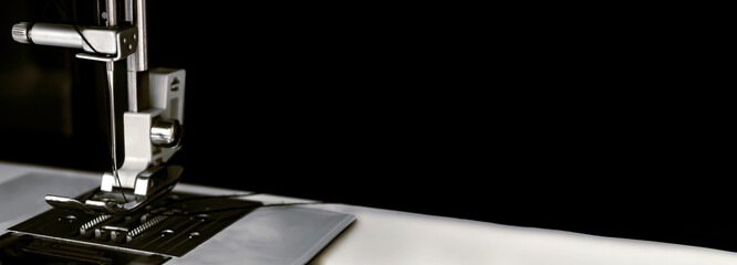 Metal needle of a white sewing machine close-up on a black background. Dark banner for sites about...