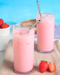 Two glasses of strawberry smoothie with metal straws in a light blue background