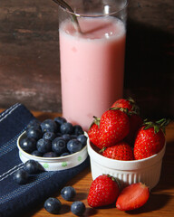Blueberries and strawberries  with a glass of strawberry smoothie in the background
