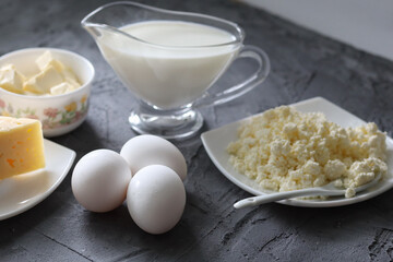 An assortment of dairy products on a wooden table in the morning for breakfast - milk, cheese, egg, yogurt, sour cream, cottage cheese and butter.