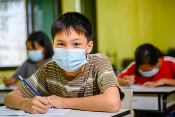Asian elementary school boy Wearing a mask to prevent coronavirus (COVID 19) doing education in a classroom at a rural school on the first day of semester.