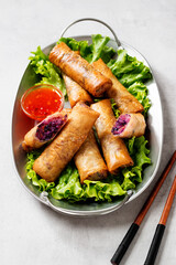Fresh fried spring rolls stuffed with red cabbage and carrot served with sweet chili dip sauce. Light gray background.