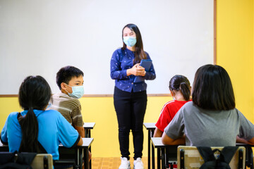 Asian female teacher and student Wearing a mask to prevent coronavirus (COVID 19) teaching elementary school students in a rural school and children talking to friends in class