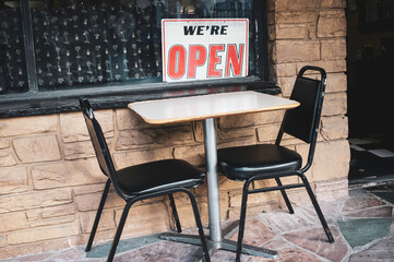 Outdoor dining area of restaurant with we're open sign on window
