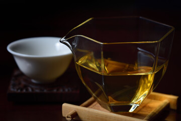 Still life of dishes for preparing a Chinese tea ceremony with a glass teapot, golden tea and a tea bowl against a dark background