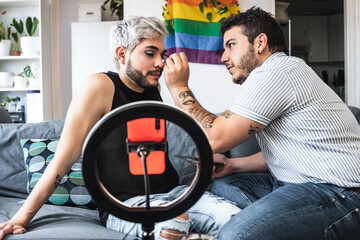 Drag queen and gay man streaming online make up tutorial with mobile phone camera indoors at home -...
