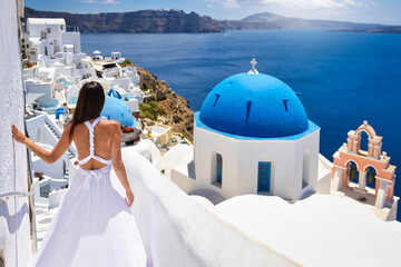 A beautiful tourist woman in a white summer dress looks at the blue domed church of the village of...