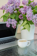 On the table are a bouquet of lilacs and a computer, a cup of coffee. Concept, work at home.