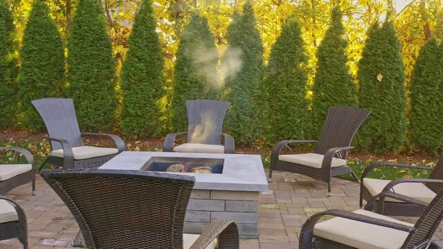 Autumn scene with contemporary fire pit in a back yard with outdoor furniture and a green fence