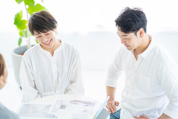 スーツ姿の女性から住宅とインテリアの説明を受ける夫婦