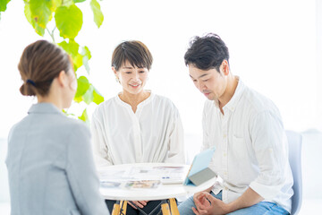 スーツ姿の女性から住宅とインテリアの説明を受ける夫婦