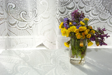 A bouquet of wildflowers in a vase of water on the table in the early morning. Flowers in the room on the table.