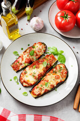 Baked eggplant with mozzarella cheese, chopped tomatoes and fresh basil leaves. Vegetarian food recipe. Light gray background.