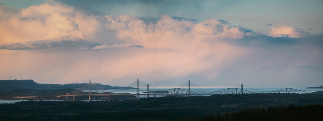 Fototapeta na wymiar Clouds at sunset over the bay and three bridges. Forth Bridges and Queensferry Crossing, Scotland, United Kingdom