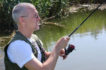 A handsome man with a cigarette in his mouth and fishing rod in hands enjoying beautiful day on the...