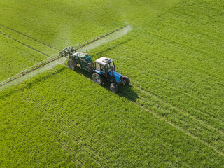 Aerial view of farming tractor spraying on field with sprayer, herbicides and pesticides at sunset....