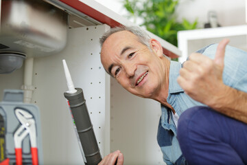 senior man holding sillicone gun and making thumbs up gesture
