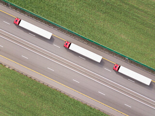 Dump trucks carrying goods on the highway. Red truck driving on asphalt road along the green...