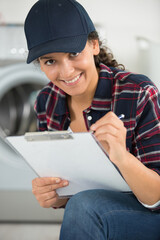 happy young female technician writing on clipboard in kitchen